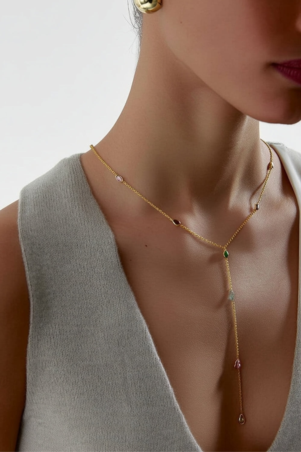 Yellow gold y-shaped lariat necklace with small multicolored rhombus gemstones worn by a model against a neutral background.