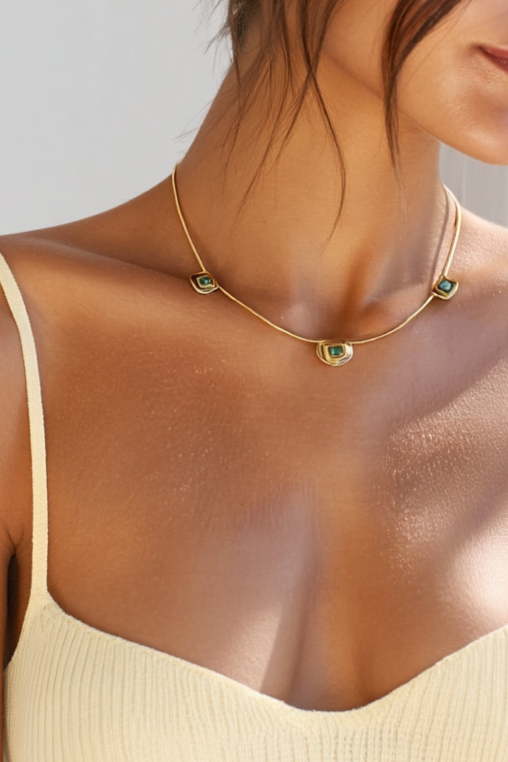 Gold Gemma necklace with green and blue gemstones and yellow gold chain worn by a model against a neutral background
