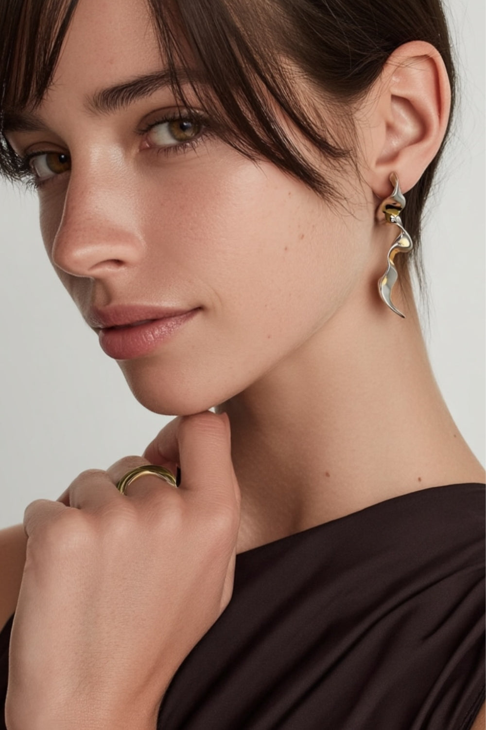 Close-up of a model wearing white gold spiral drop earrings with an abstract design.