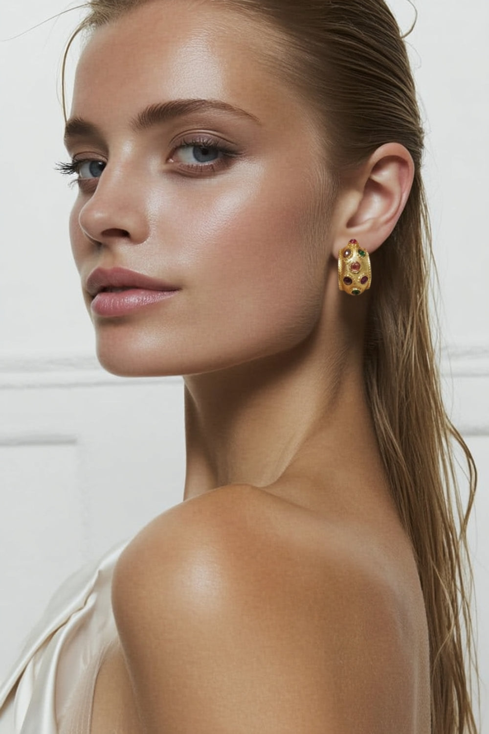 Close-up of a model wearing yellow gold earrings with multicolor colorful gemstones.
