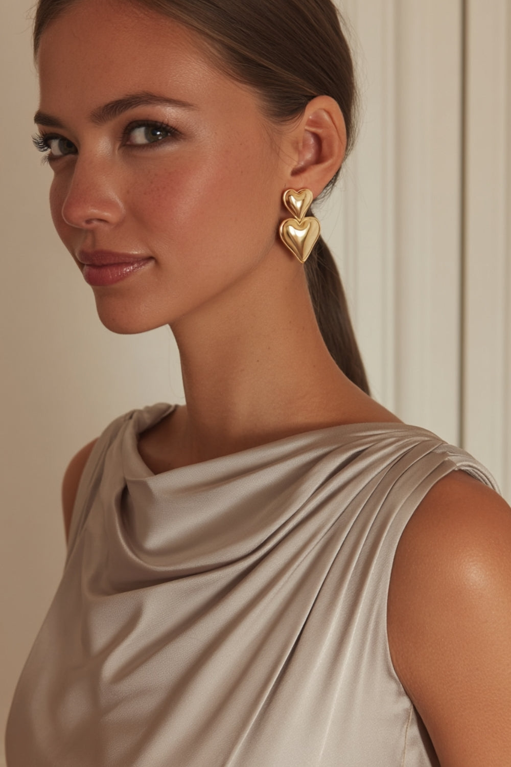 A model wearing yellow gold double heart-shaped drop earrings.