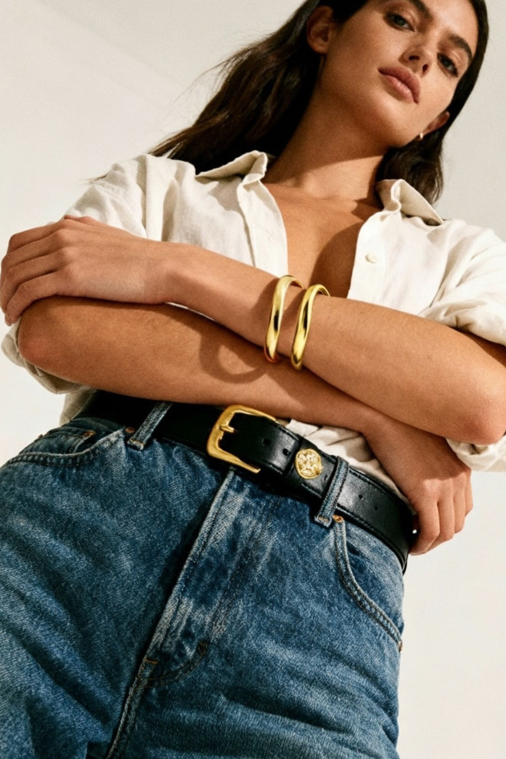 Woman wearing a white shirt, blue jeans, and two double cuff curved bangle bracelets.