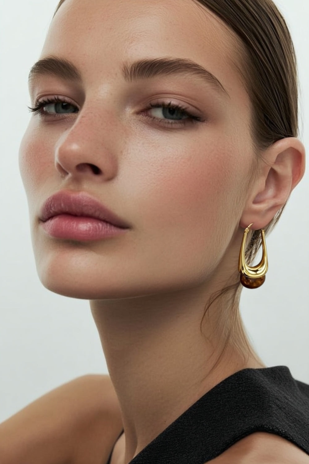 Model wearing yellow gold hoop earrings with brown stone bottom accent on a white background.