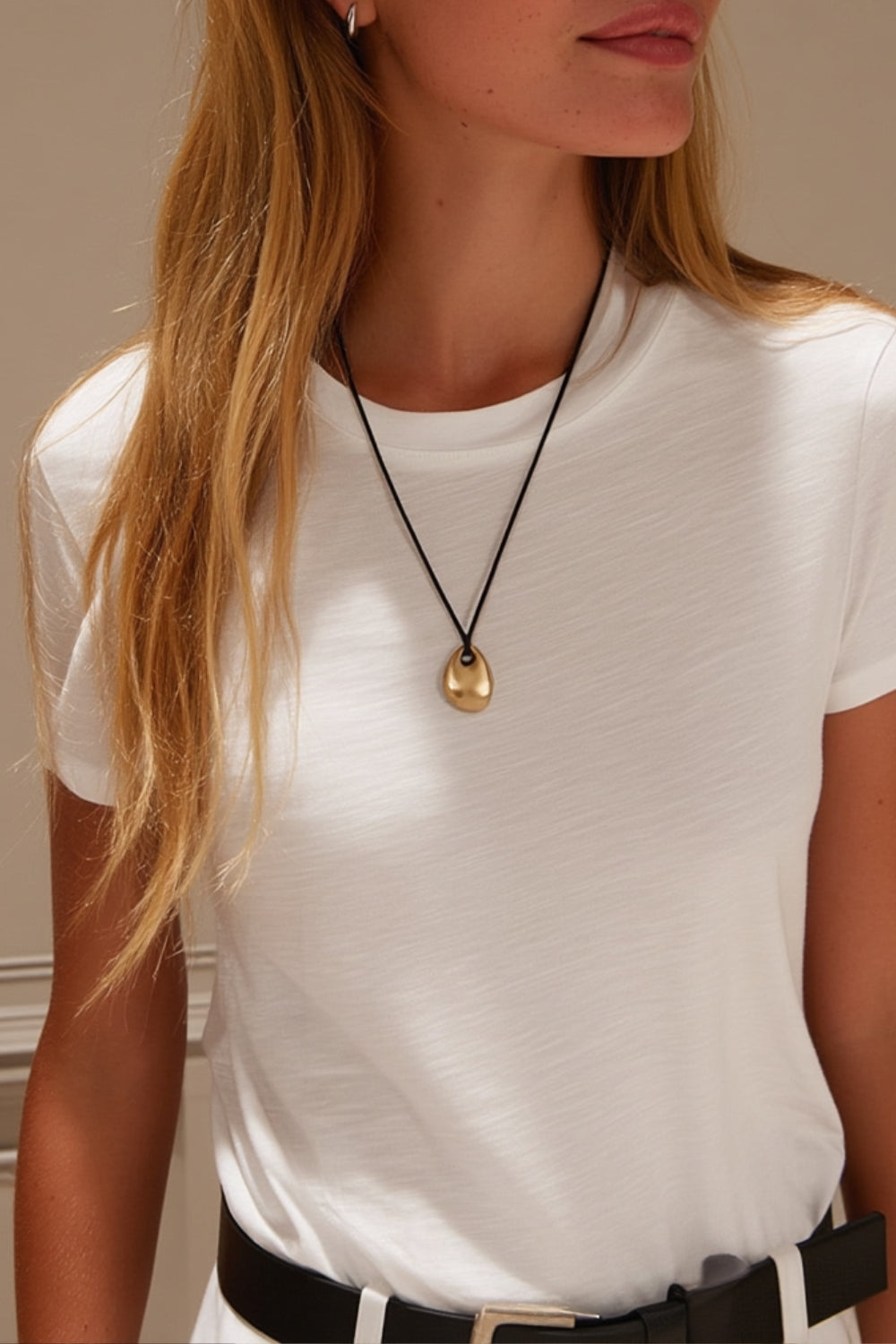 model wearing an abstract shape yellow gold pendant necklace with black cord on a white background.