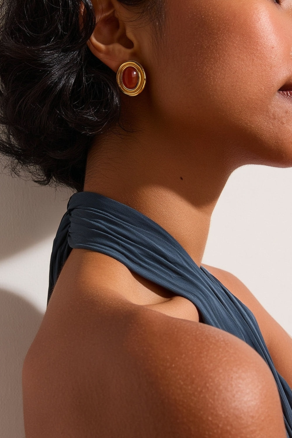 Close-up of a model wearing yellow gold earrings with red stones against a neutral background